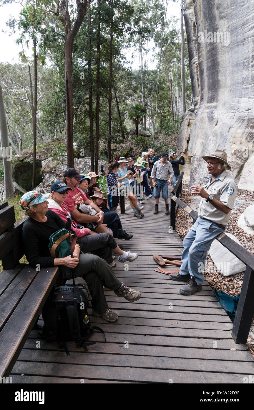 Ein Eingeborener Reiseleiter gibt ein Gespräch auf dem Hintergrund der gut erhaltenen Aboriginal Rock Art Schablone für die Besucher. Die Schablone Art Site wird geglaubt, t Stockfoto