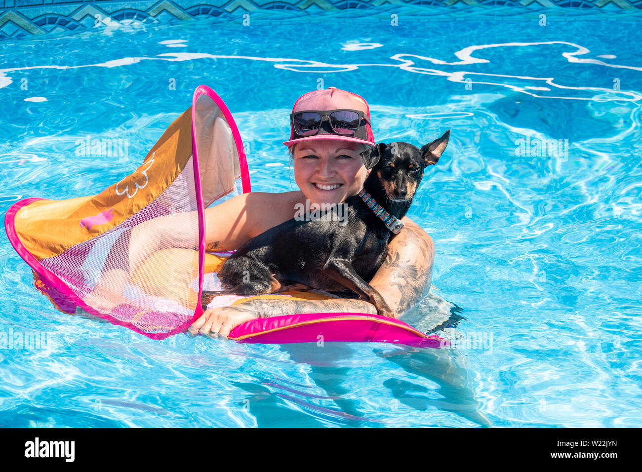 Kaukasische Frau entspannende mit schwarzen pinscher Hund auf einer Flotation Gerät im Schwimmbad Stockfoto