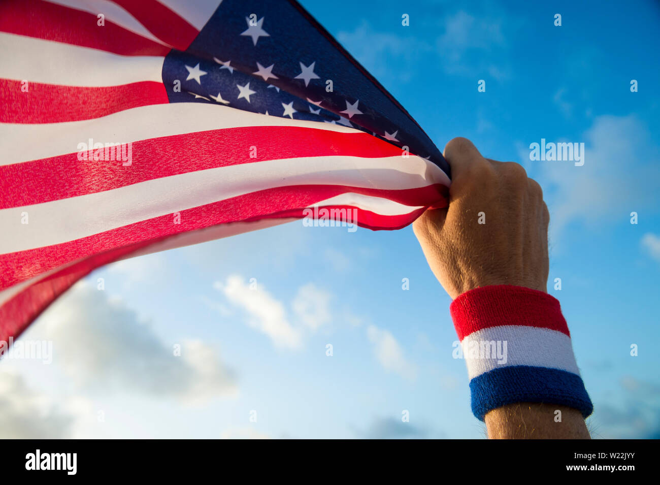 Patriotische hand mit USA rot, weiß und blau Armband Holding eine amerikanische Flagge schwenkten in goldenen sonnigen blauen Himmel Stockfoto
