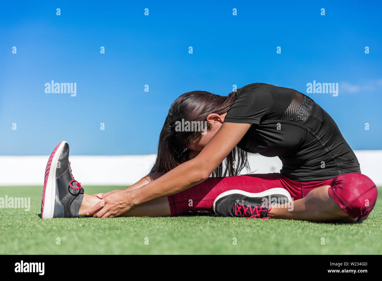 Fitness Frau zurück reicht und Beinmuskulatur mit TOE-touch erstreckt. Sportliche jungen Athleten ein ein Bein nach vorne sitzt Yoga Stretch auf im Gras biegen. Sitzung Kopf zu Kniebeuge über darstellen. Stockfoto