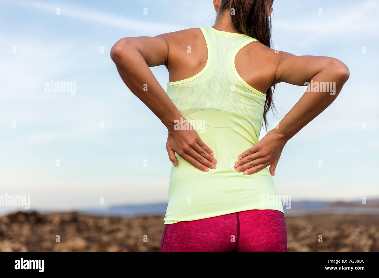 Trail Running Runner mit schmerzhaften Rückenschmerzen Verletzungen oder beanspruchten Muskelfasern in der Nähe der Wirbelsäule. Weibliche Athleten hinter im freien Lauf die Taste Körper mit Händen für Muskeln Muskelkater einzwängen. Stockfoto