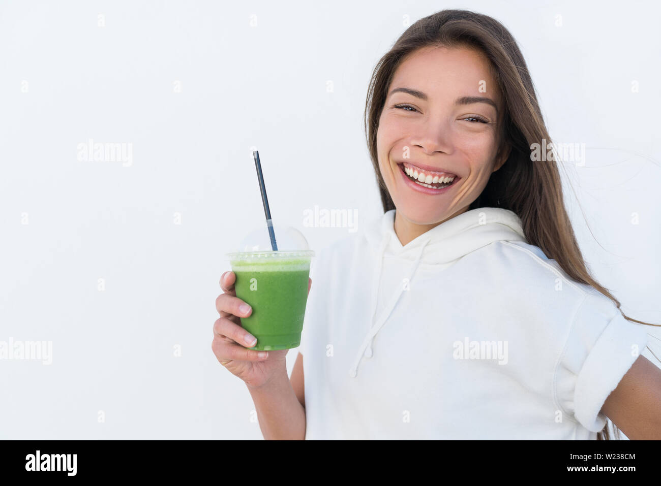 Gerne asiatische Frau trinken gesunden grünen Spinat smoothie Cup detox für Gewicht-Verlust-Diät. Junge lächelnde Fitness sportliche Mädchen mit Gemüse Saft trinken von Saft bar Gesundheit trend, weisser Hintergrund. Stockfoto