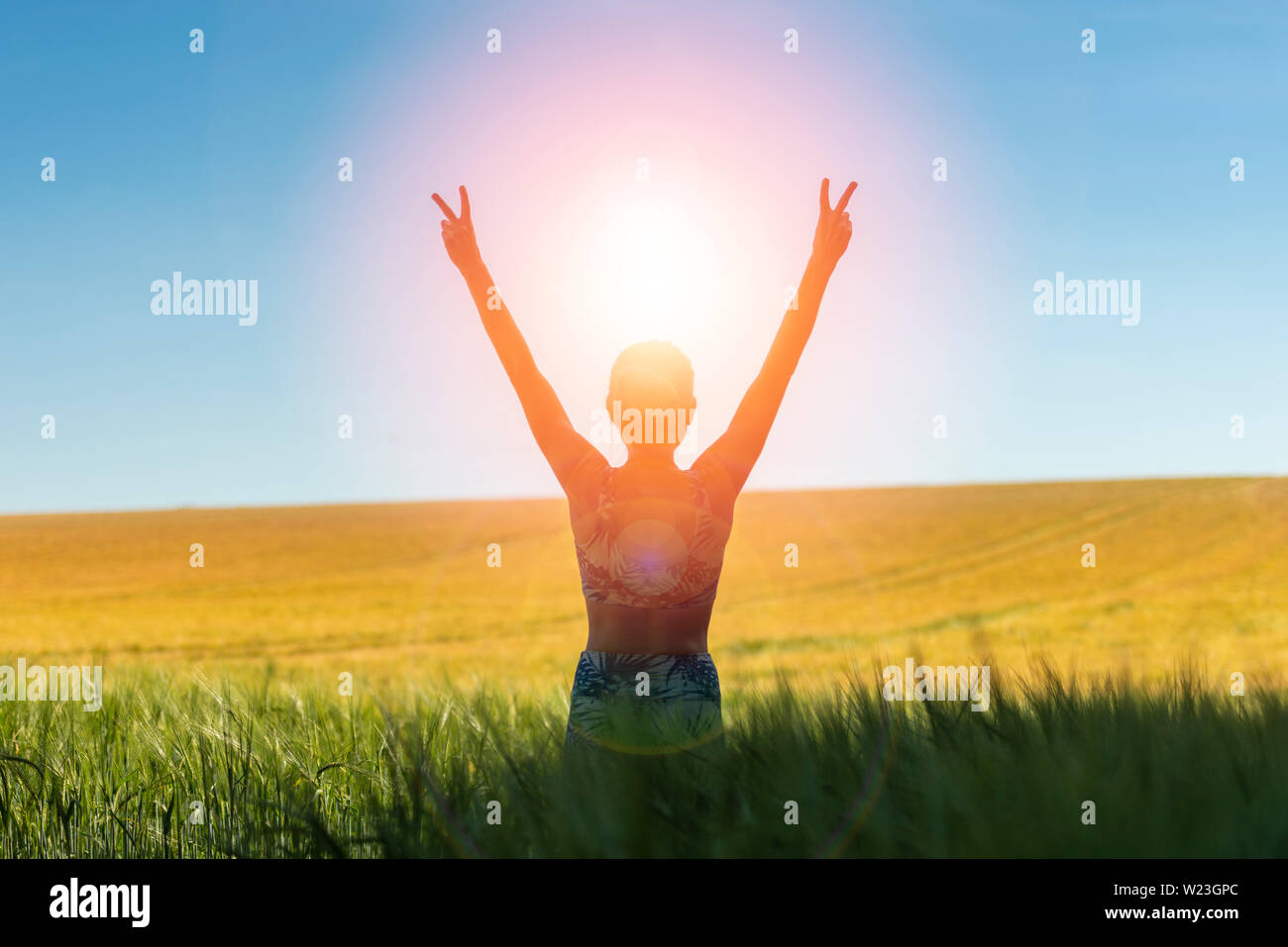 Rückansicht einer Frau bei Sonnenaufgang mit ihren Armen in der Freude und Freiheit stehen in einem Feld von Weizen angehoben Stockfoto