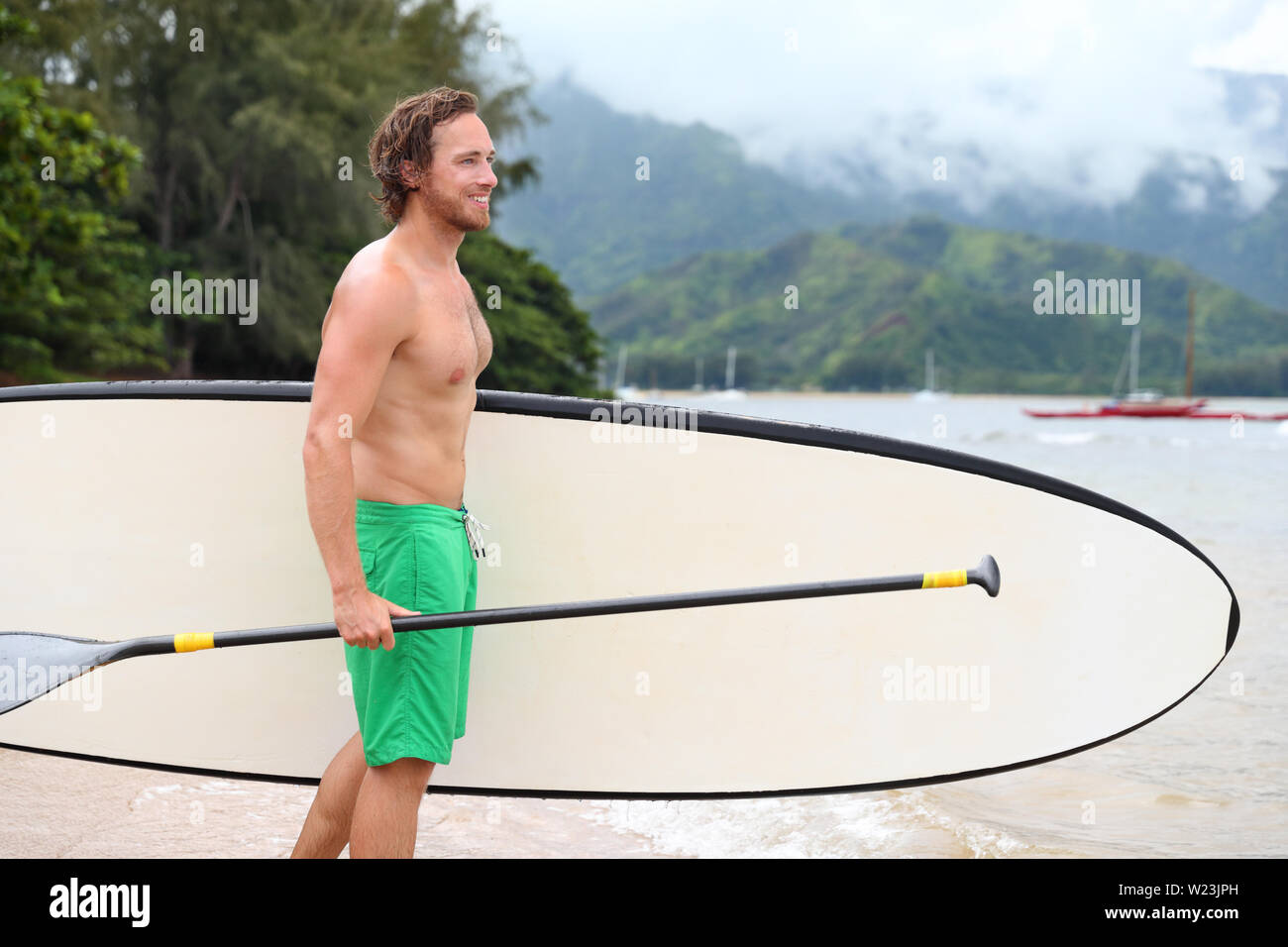 Stand Up Paddle Board Strand Mann tun paddleboarding Paddleboard gehen in Hawaii. Junge kaukasier männlichen Athleten auf Hawaiian Beach auf Sommerferien urlaub reisen. Stockfoto