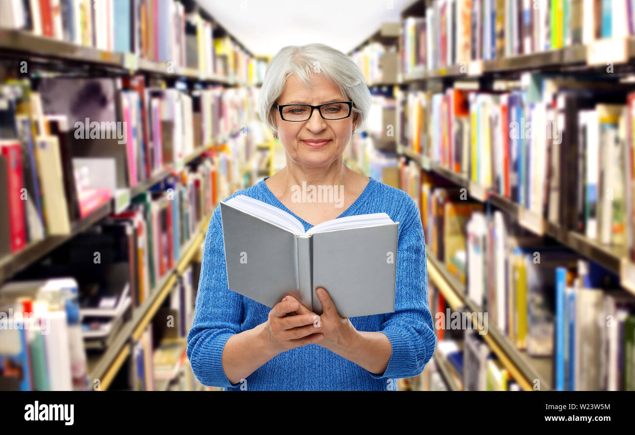 Ältere Frau in Gläser Buch an der Bibliothek Stockfoto