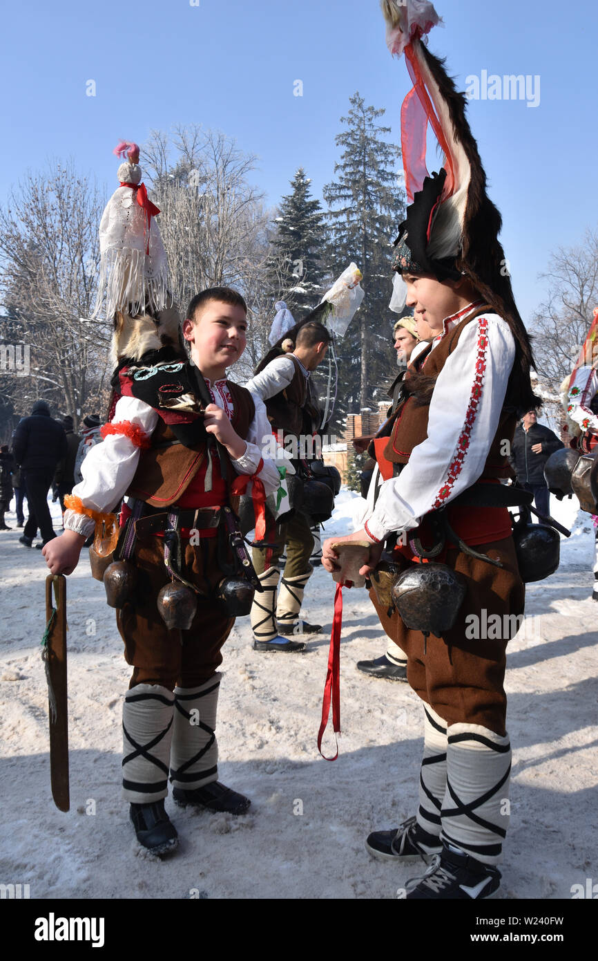 Razlog, Bulgarien - 12. Januar 2019: Zwei in bulgarischen Volkstrachten gekleidete Jungen auf der verschneiten Straße beim Volksfest in Starchevata und Maskerade Stockfoto