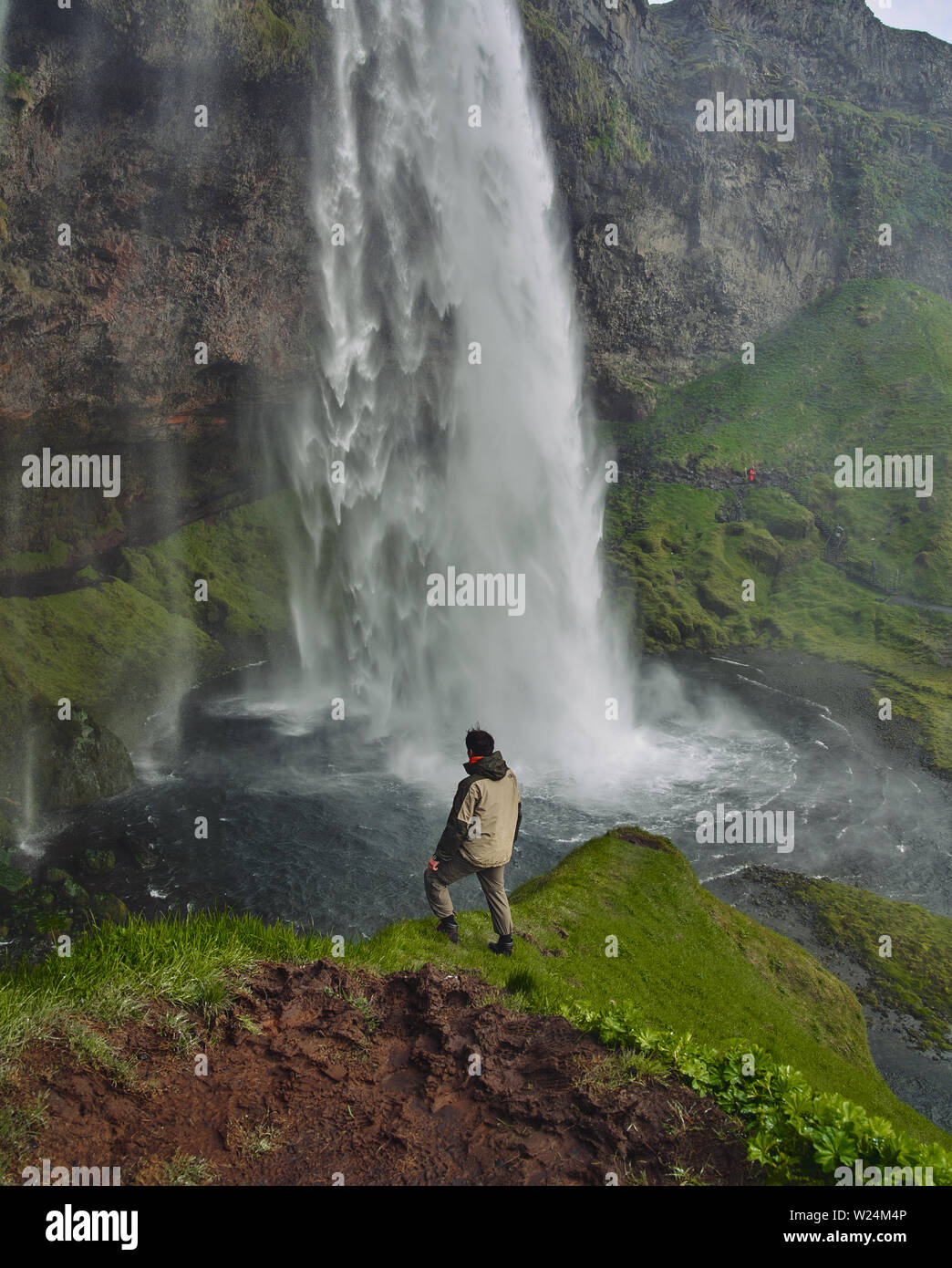 Gljufrafoss Wasserfall in der Schlucht der Berge. Touristische Attraktion Island in der Nähe des Seljalandsfoss. Mann Wanderer in blaue Jacke stehen auf Stein und sieht am Fluss des fallenden Wassers Stockfoto