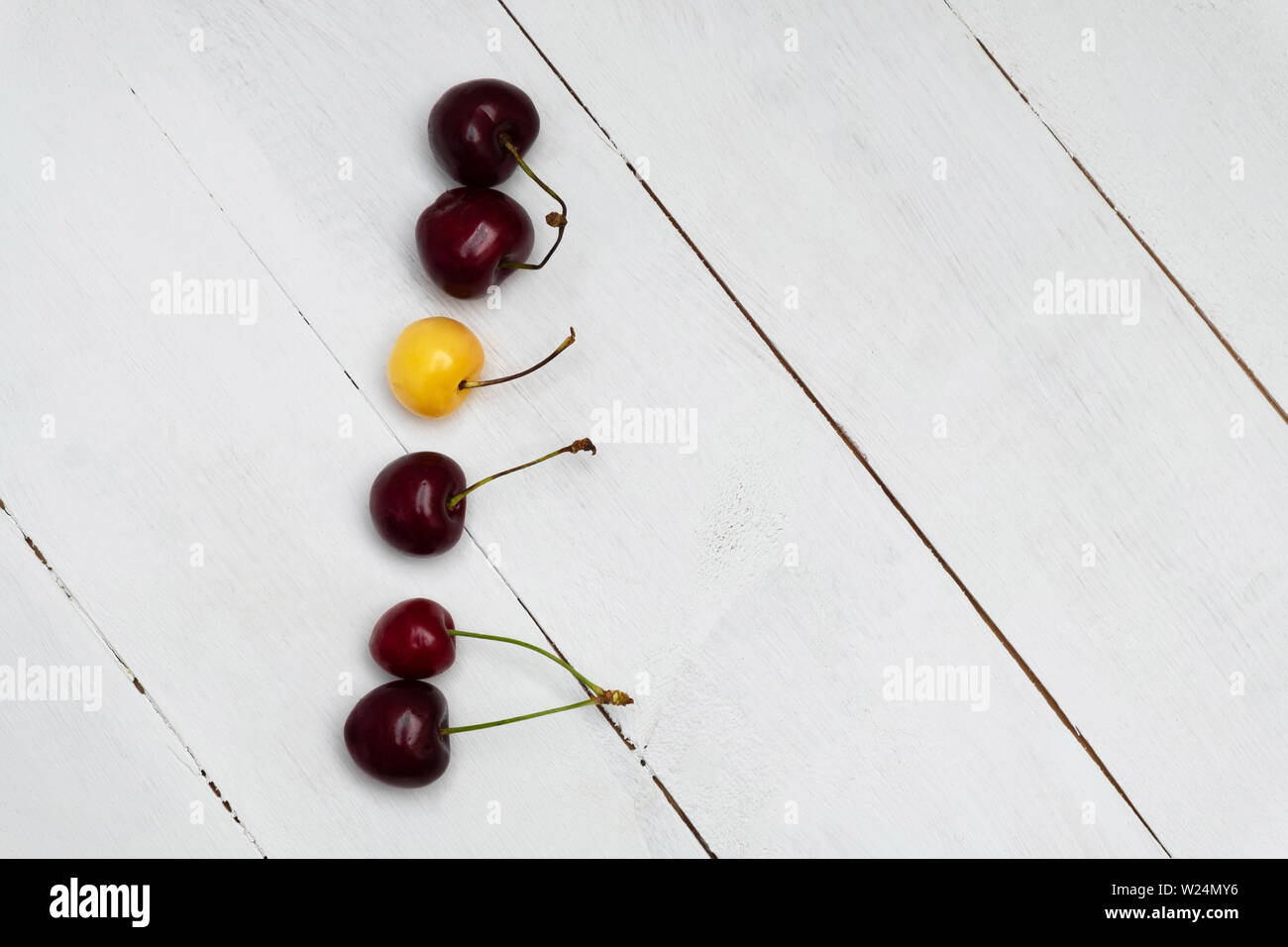 Weiß cherry unter roten Kirschen auf Holz- Hintergrund. Um sich von der Masse ab, Individualität und Differenz Konzept Stockfoto