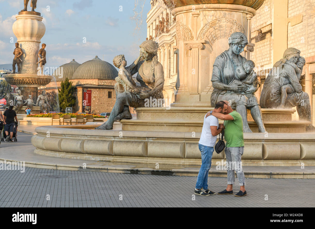 SKOPJE, MAZEDONIEN/22. AUGUST 2018: Zwei Fußgänger in der Nähe der Statuen und Brunnen auf der Ostseite der Brücke aus Stein, Skopje City Center umfassen Stockfoto