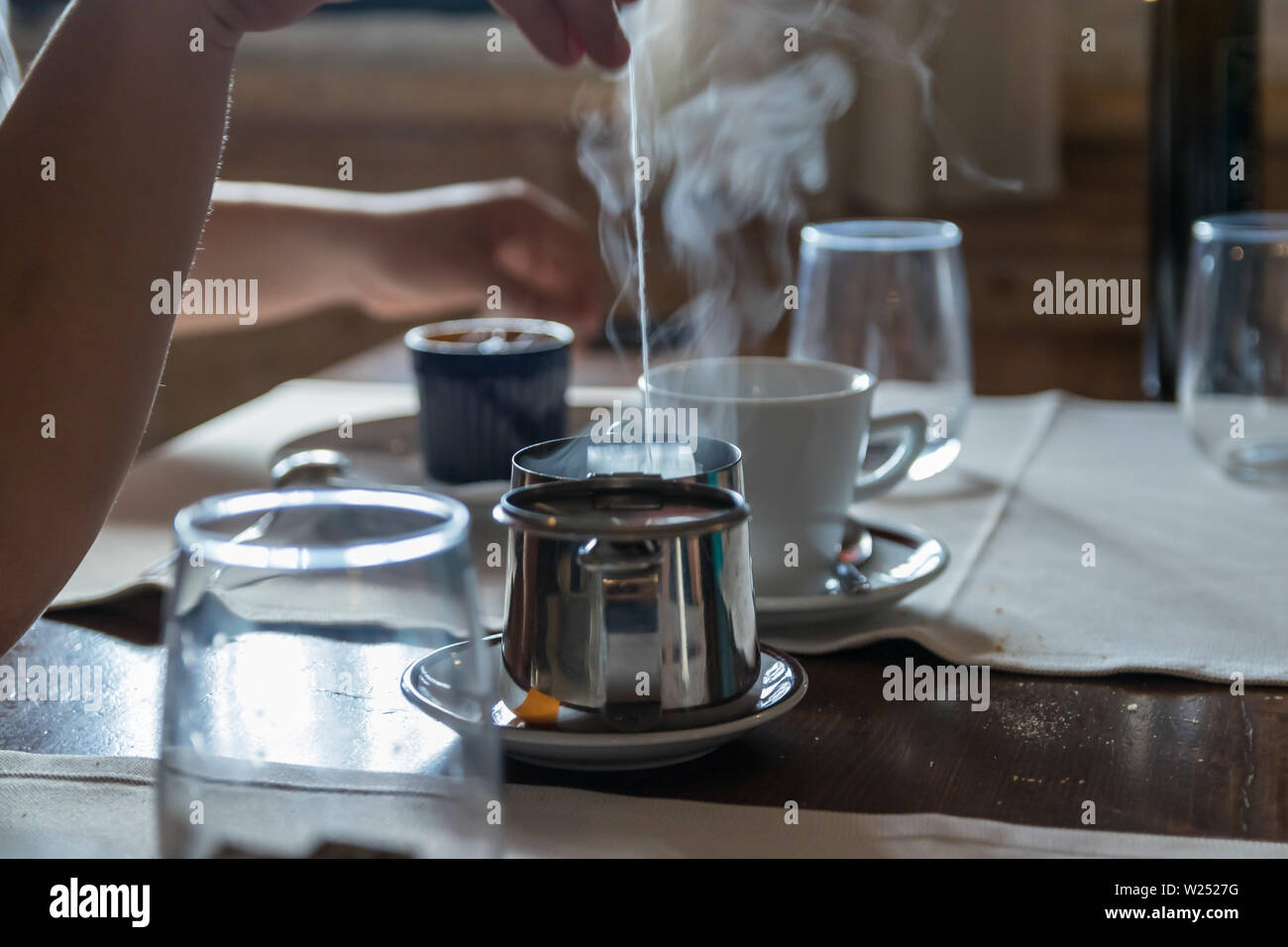 Kleine Teekanne mit Teebeutel, einige Gläser auf dem Tisch im Restaurant. Weißer Dampf steigt über heißes Wasser. Selektive konzentrieren. Stockfoto