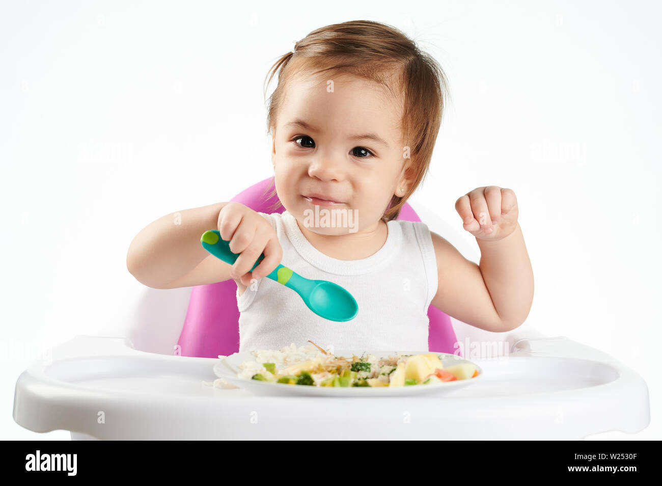 Cute Portrait von Baby Mädchen mit Löffel auf Hoher Stuhl isoliert Stockfoto