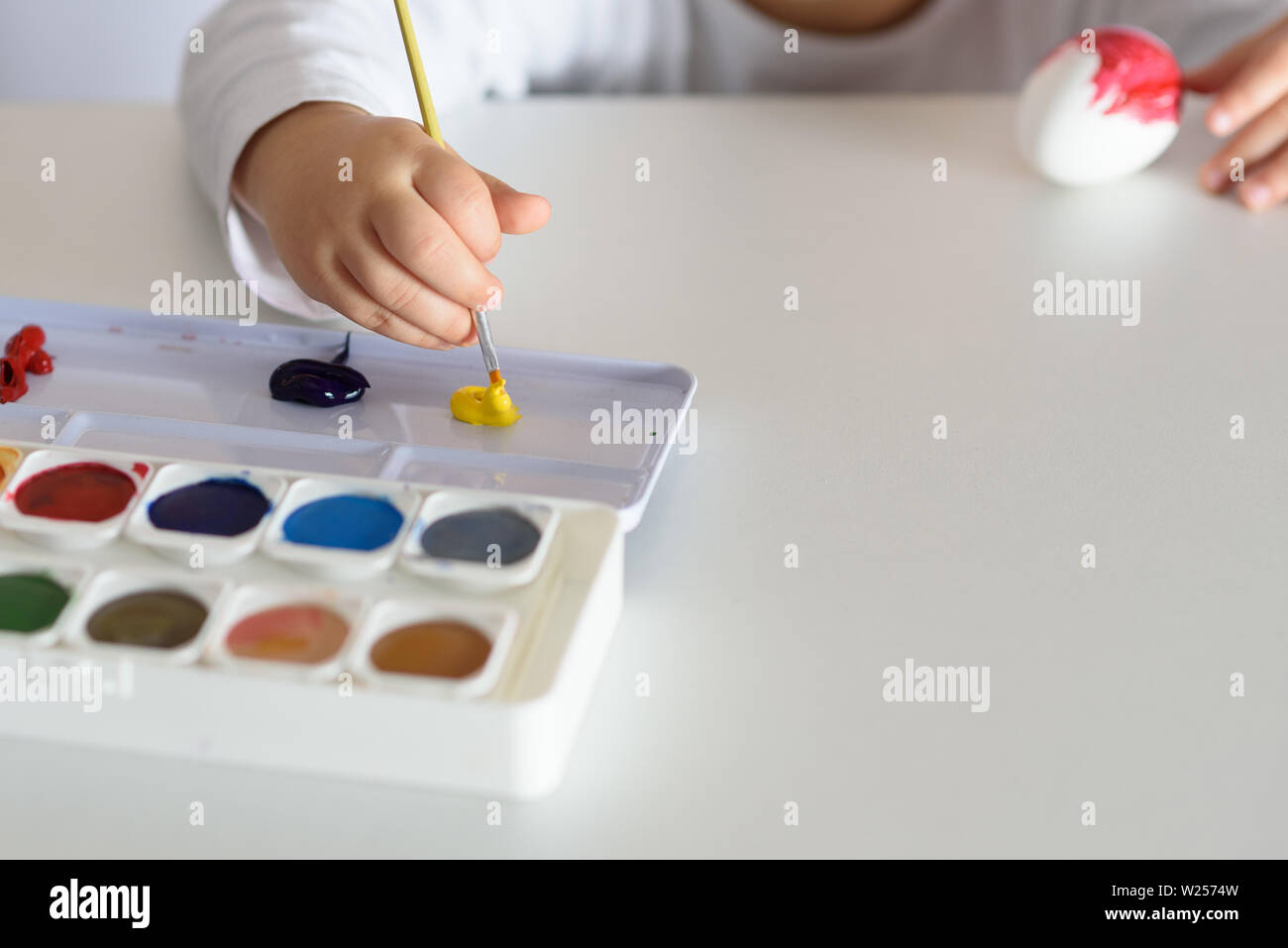 Kind Hände bemalte Ostereier, Farben und Pinsel auf weißer Tisch. Die Vorbereitung auf das Osterfest. Kid Hände zeichnen mit Farben. Stockfoto
