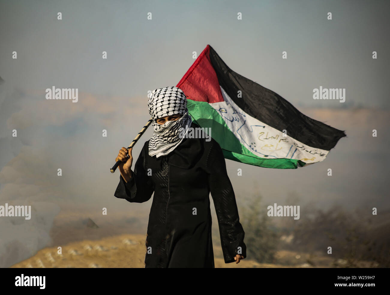 Gaza, Palästina. 05. Juli, 2019. Eine palästinensische Frau trägt die palästinensische Flagge mit in einem Schwall von Tränengas während einer Demonstration für ein Ende der Belagerung des Gazastreifens im südlichen Gazastreifen verhängt. Credit: SOPA Images Limited/Alamy leben Nachrichten Stockfoto