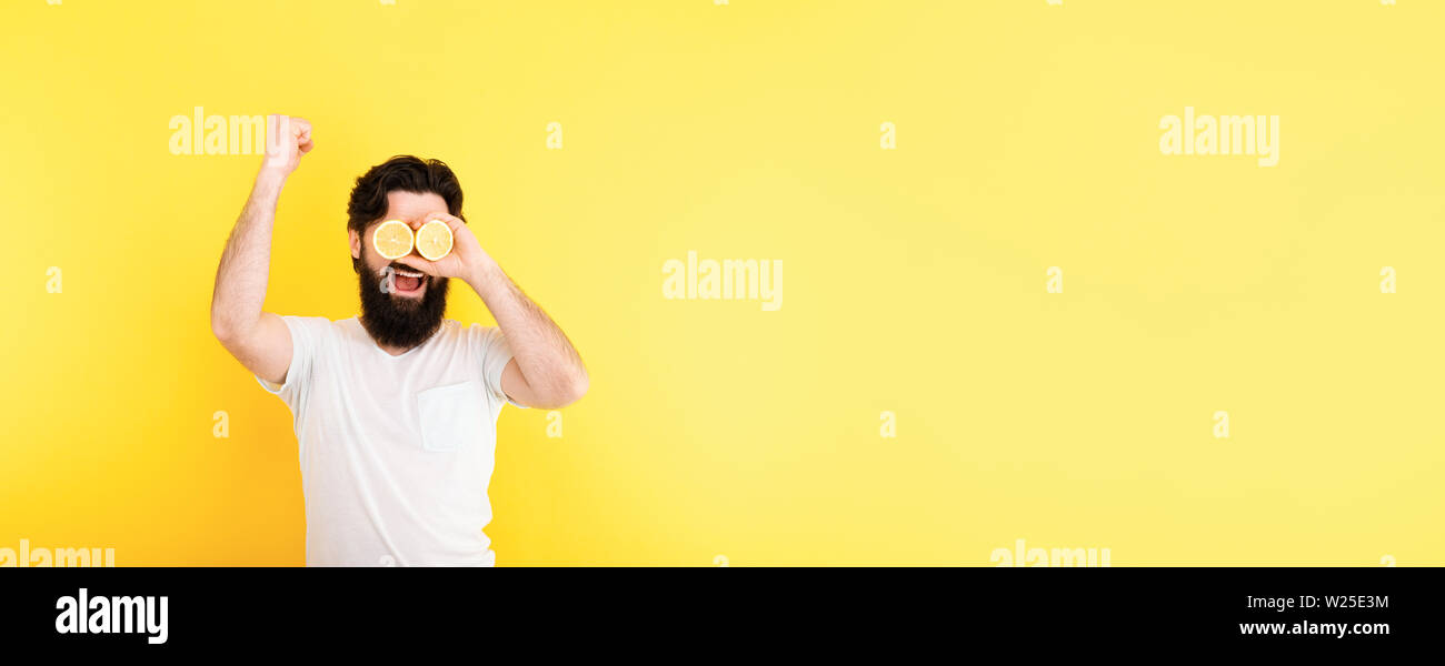 Bärtiger hippie Mann mit Zitronenscheiben vor Augen, auf gelben Hintergrund, Panoramic Image Stockfoto