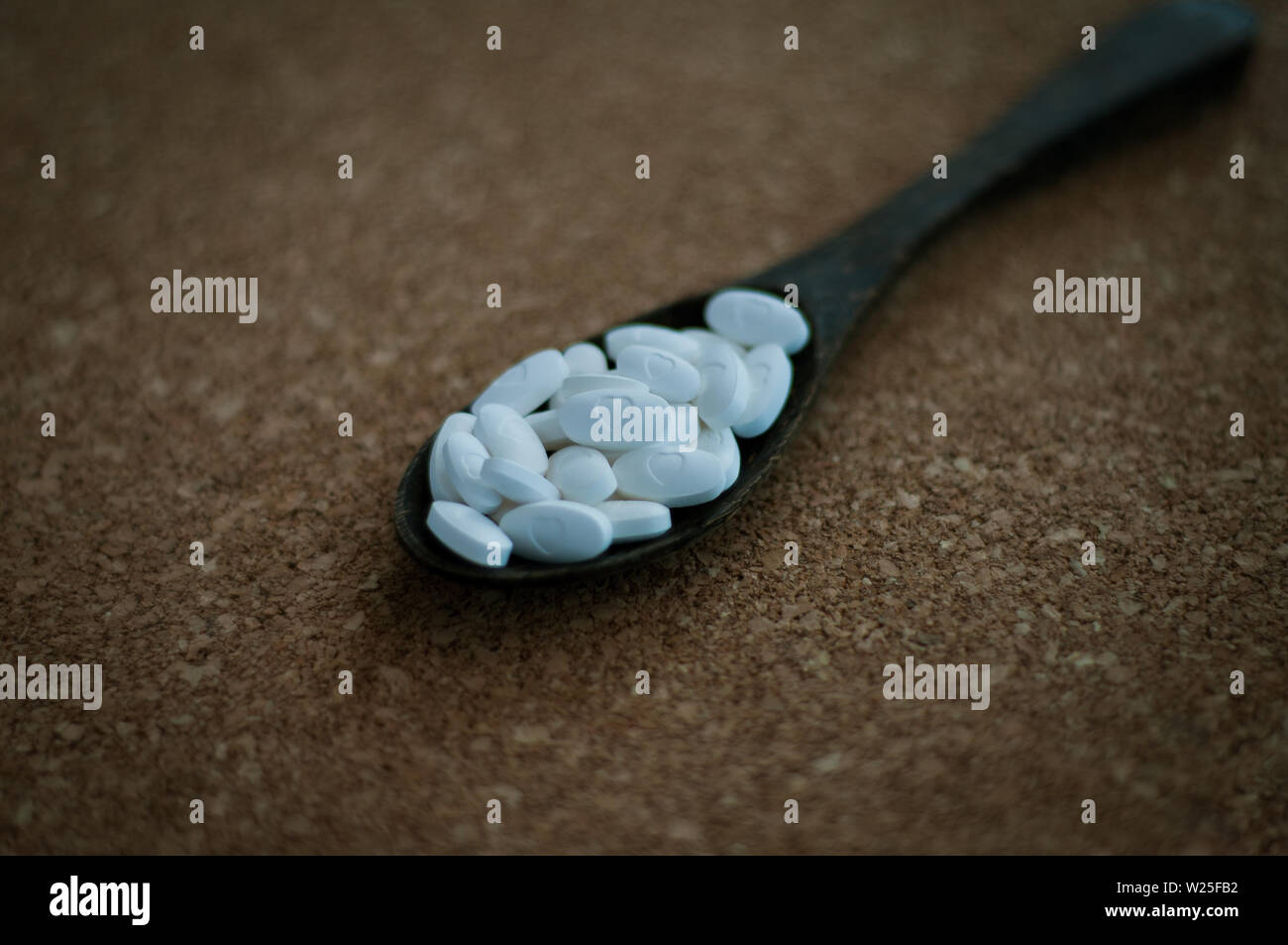 Weiß pharmazeutischen Pillen und Medikamente in den Löffel aus Holz auf einem braunen Kork. Valentines, Herz, Krankheit, Gesundheit und Heilung. Stockfoto