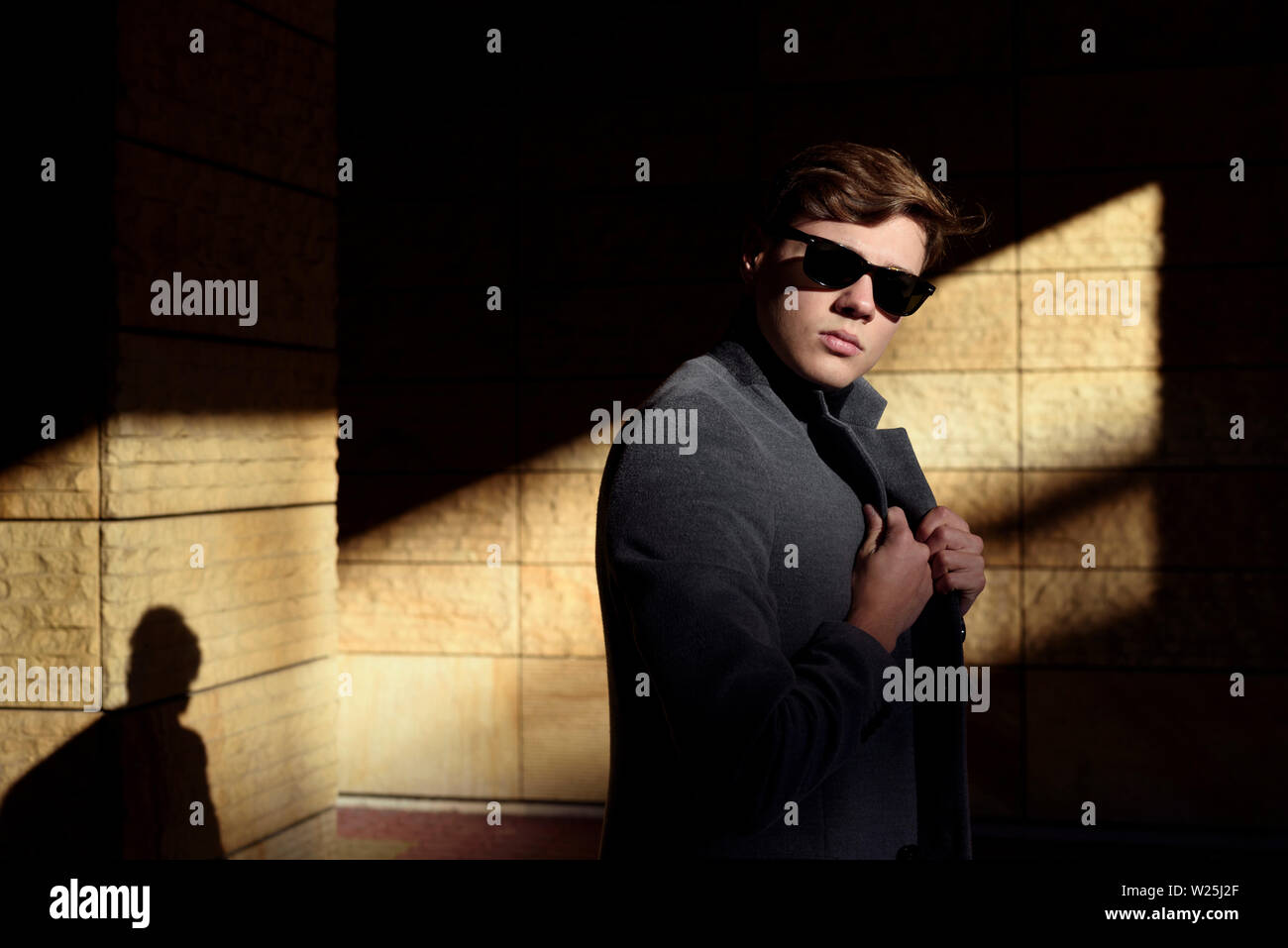 Stilvolle Mann im Sonnenlicht und Schatten posieren, in Smart Casual Jacke und Sonnenbrille gekleidet. Fashion Concept. Stockfoto