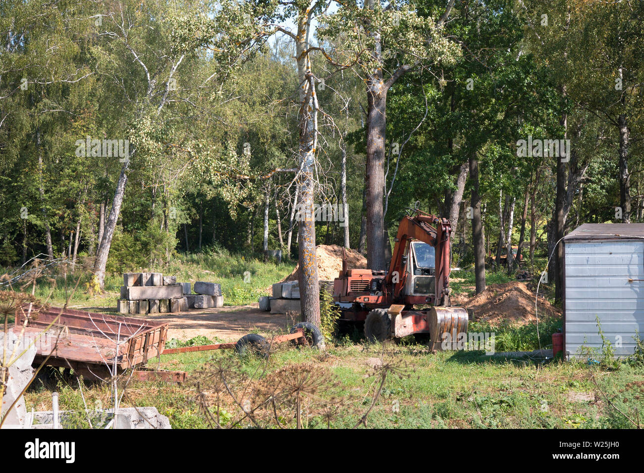 Erstellung einer Website im Wald für den Bau eines eigenen Hauses. Bagger, kleine Bagger für den Bau eines Hauses Stiftung arbeitet Stockfoto