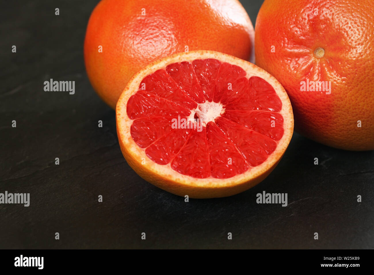 Rosa Grapefruits halbieren, ganze Zitrusfrüchte im Hintergrund auf dem Schwarzen Brett Stockfoto