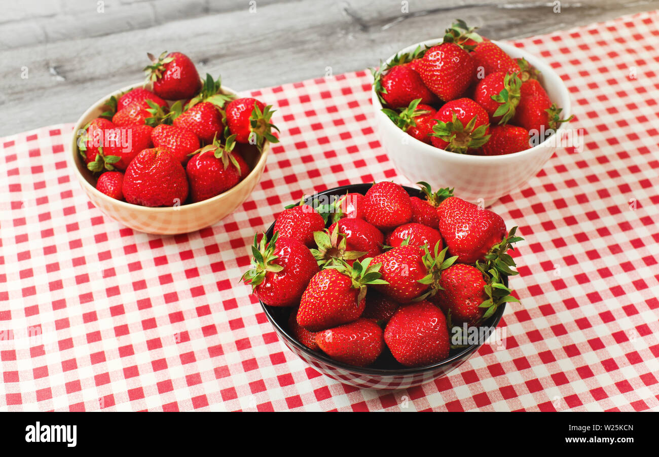 Drei kleine Schalen mit reifen Erdbeeren auf dem Schreibtisch mit rotem gingham Muster Tischdecke Stockfoto