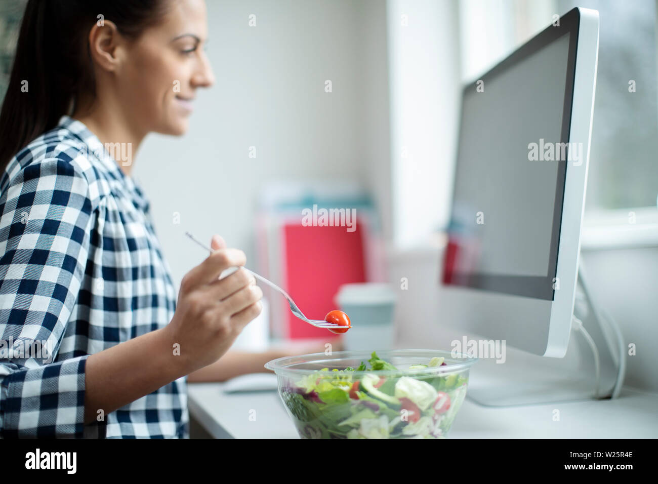 Mitarbeiterin im Büro in gesunden Salat Mittagessen am Schreibtisch Stockfoto