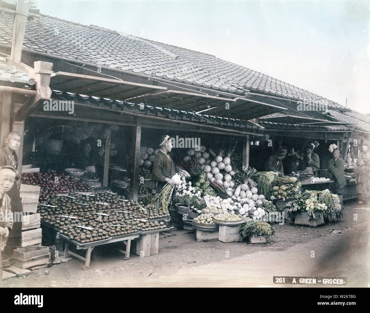 [1880s Japan - Japanische Gemüse Store] - Der Inhaber einer pflanzlichen Store ist ein sehr großer Kabu (Rübe). Klette, Rettich, Senf und Zwiebeln können vor ihm gesehen werden. Panels an der Traufe geschickt werden die Produkte aus dem Sonnenlicht zu schützen. 19 Vintage albumen Foto. Stockfoto