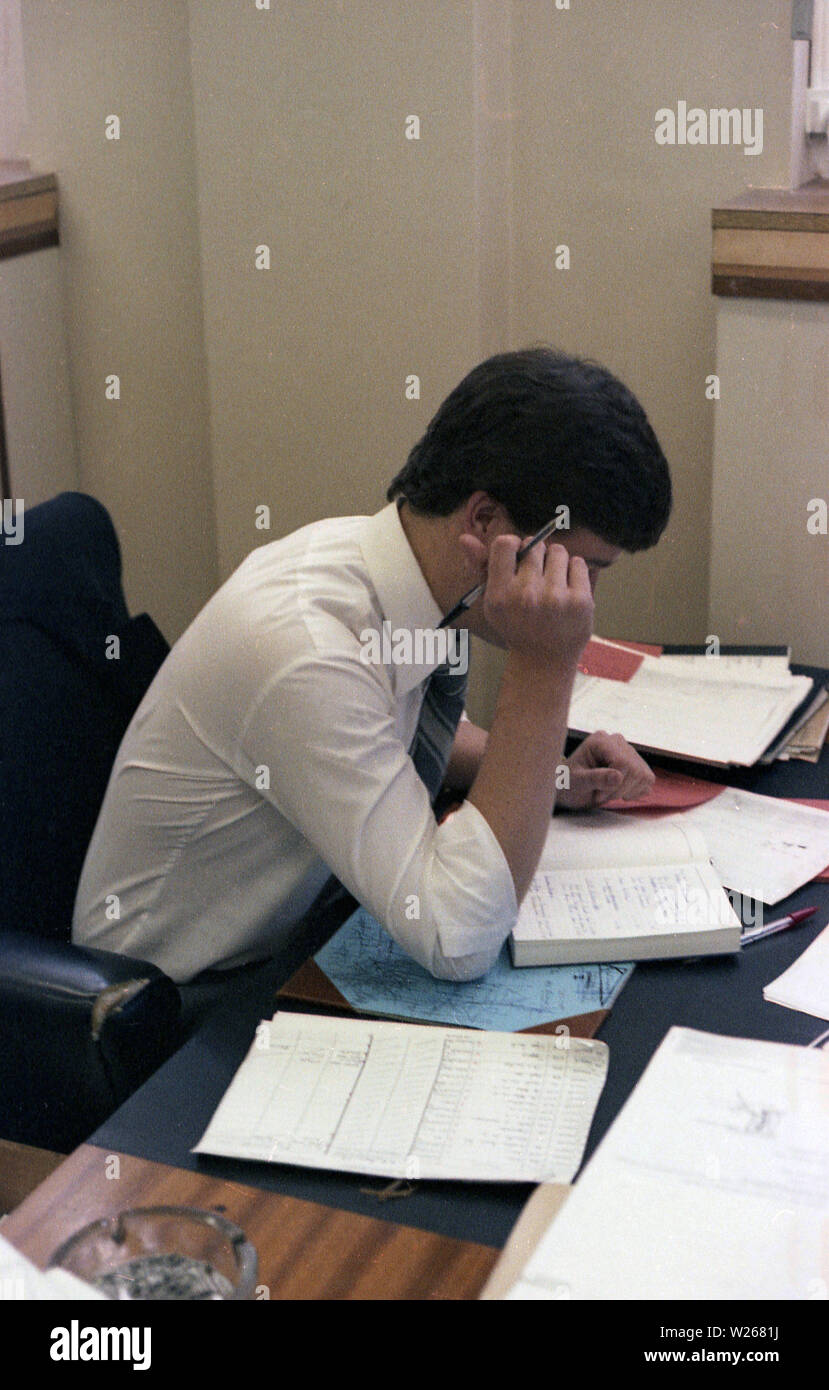 1970 s, historischen, ein Mann, Anfang der 30er Jahre, Sitzen, Woking in einem Büro, einer Finance Manager oder möglicherweise ein Buchhalter in Anbetracht der Schreibarbeit und Zeitschriften auf dem Schreibtisch. Stockfoto