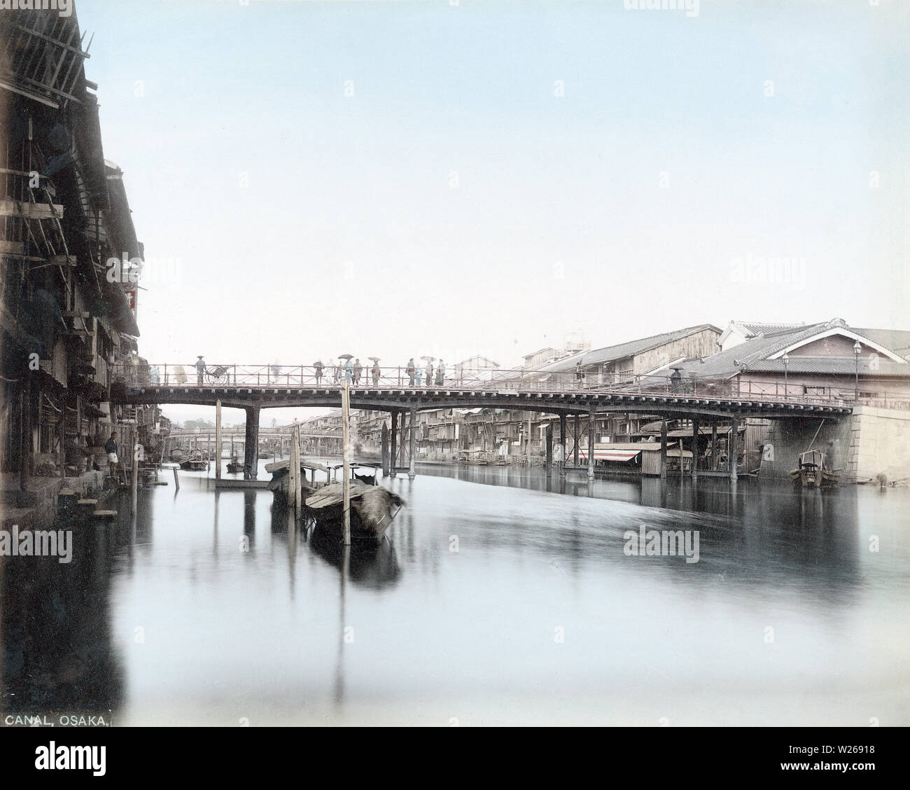 [1880s Japan - Dotonbori Canal, Osaka] - Die Dotonbori Kanal und Ebisubashi (ebisu Brücke) in Osaka's berühmten Vergnügungsviertel. Holz- teehäuser Masse der linken Seite des Kanals. Italienische geborene Fotograf Adolfo Farsari shot dieses Foto irgendwann zwischen 1877 (Meiji 10) und 1887 (Meiji 20) nach Osten. Zu dieser Zeit erlebte die Stadt ein hohes Maß an Wohlstand als durch die Anwesenheit von Gas Lampen auf der rechten Seite der Brücke gesehen werden kann. 19 Vintage albumen Foto. Stockfoto