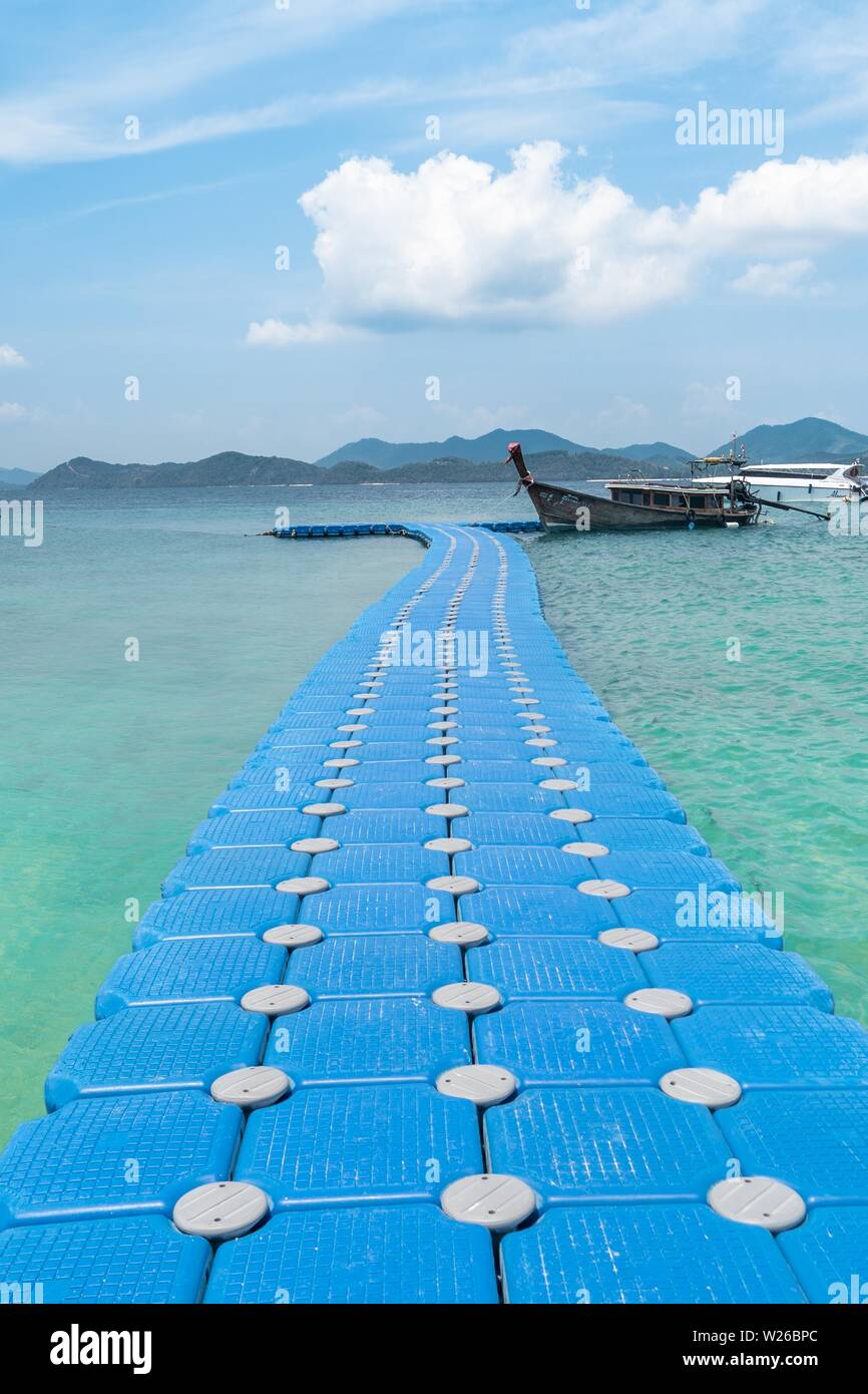 Schuss von blauen Kunststoff-Dock schwimmt über das Meer mit Ein Holzschiff parkte daneben Stockfoto