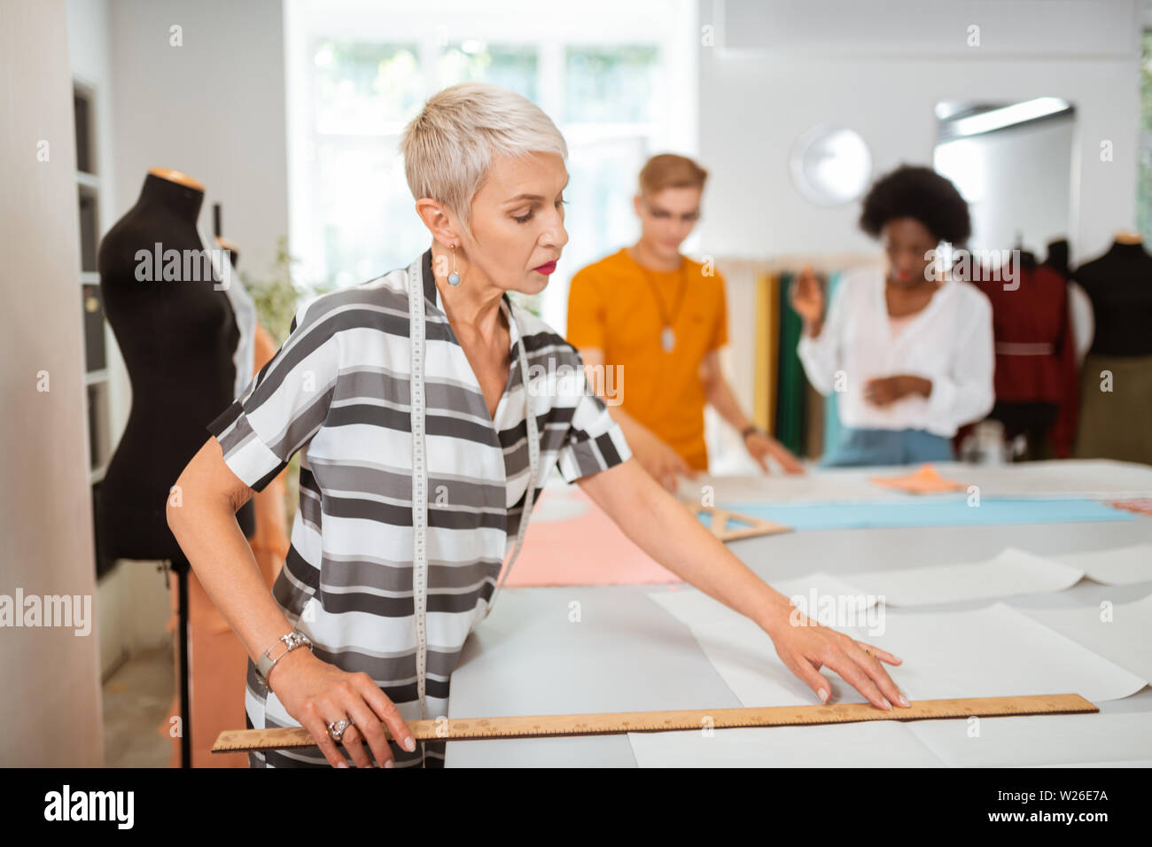 Messung ein Muster. Stilvolle kaukasische Frau Schneider stehen in einem Studio bei der Messung einer Papier Muster mit einem Lineal Stockfoto