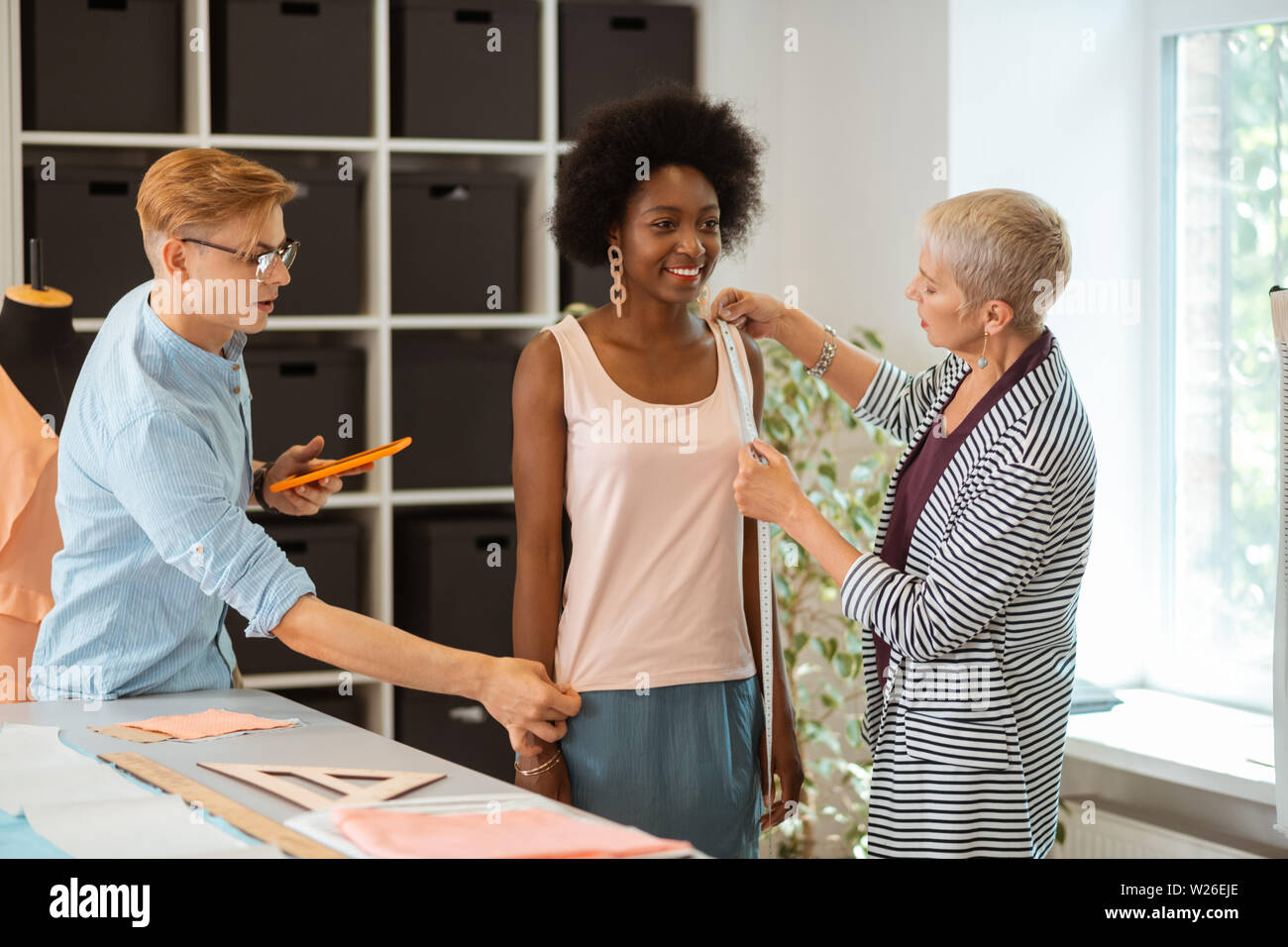 Die Kleidung Messungen. Gerne Modell stehen in der Gesellschaft von zwei Fashion Designer ihre Messungen unter Stockfoto