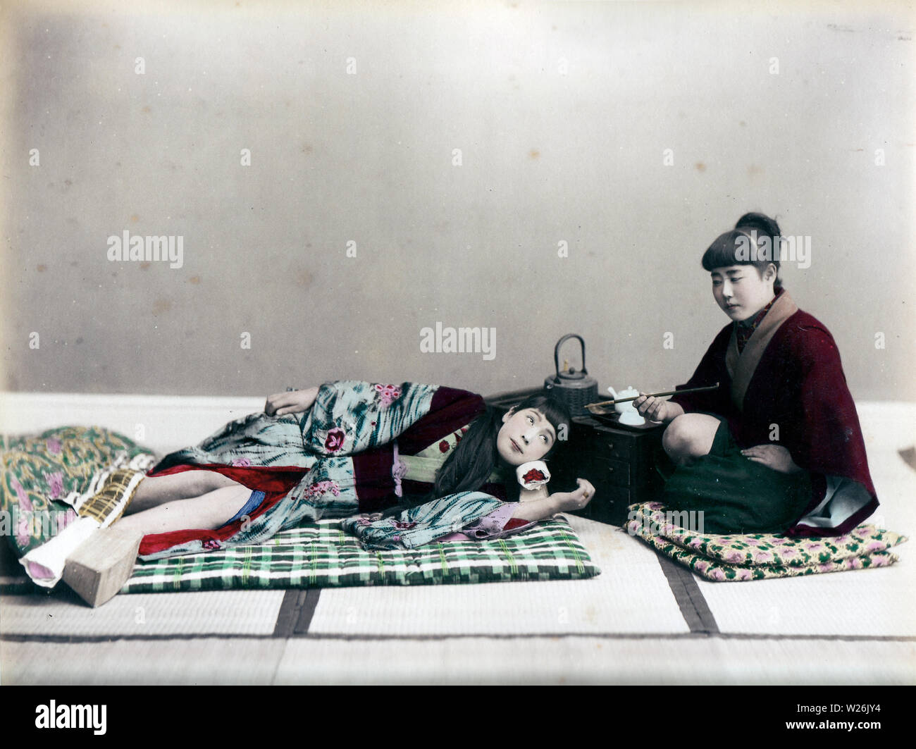 [1890s Japan - Japanische Frau Schlafen] - ein Frauen liegt auf einem Futon, während andere eine kiseru Rohr in einer Einstellung Studio hält. 19 Vintage albumen Foto. Stockfoto