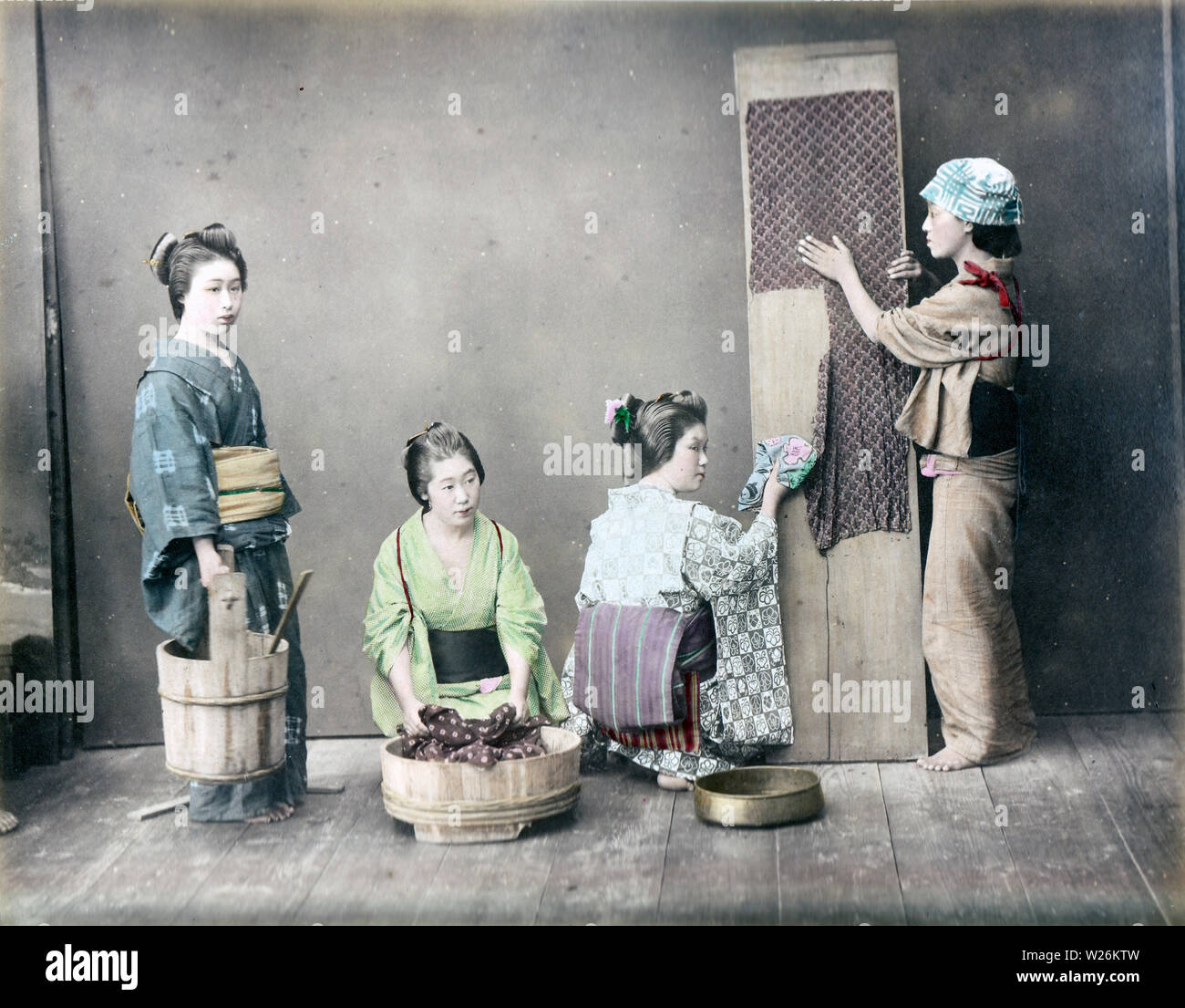 [1890s Japan - Japanische Frauen Waschen] - vier Frauen im Kimono und traditionellen Kopfbedeckungen sind die Wäsche machen. Die Frau in der Mitte ist das waschen Kleidung in einer Oke (hölzerne Schaufel), während eine Frau auf der rechten Seite ist ein Stück Textil Verbreitung auf einem Holzbrett. 19 Vintage albumen Foto. Stockfoto