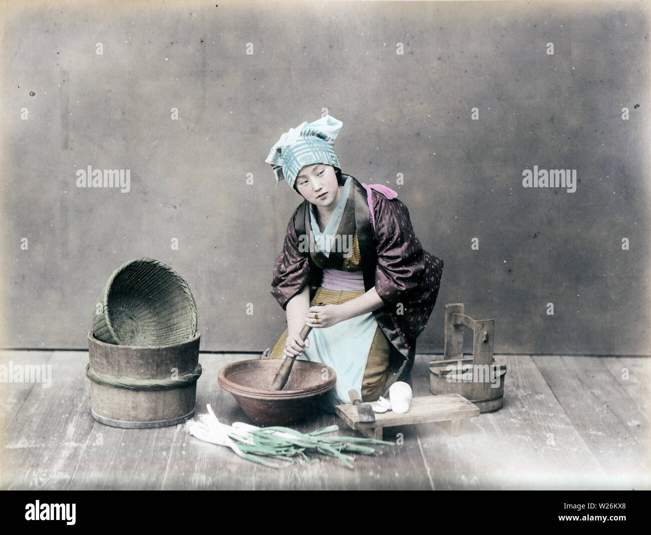 [1890s Japan - Japanische Frau Kochen] - In diesem Studio Foto der täglichen Küche arbeiten, eine Frau im Kimono ist das Schleifen etwas in einem suribachi (Mörtel). Auf der linken Seite ist ein Oke (hölzerne Schaufel), während auf der rechten daikon Rettich (Japanisch) auf einer hölzernen cutboard gesehen werden kann). 19 Vintage albumen Foto. Stockfoto