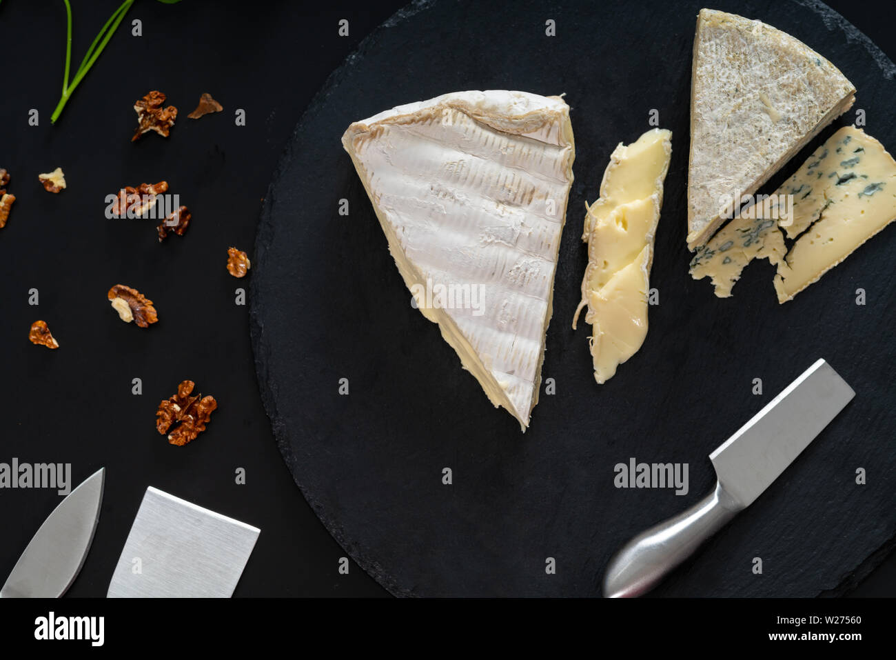Auswahl der semi-soft Käse auf einem Brett mit einem käsemesser und gehackte Walnüsse von oben gesehen auf Schwarz in einem flachen lag noch Leben Stockfoto