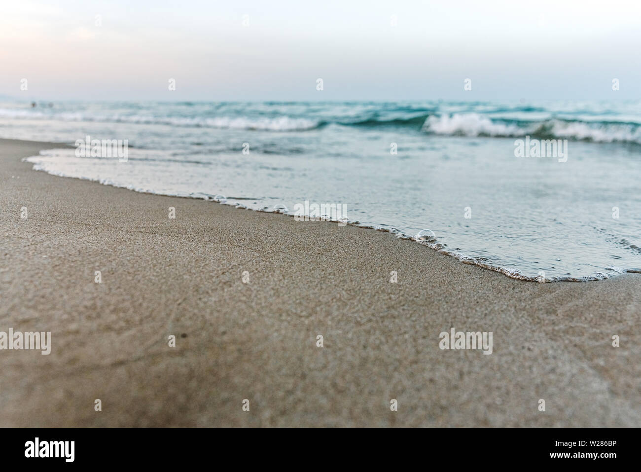 Kleine Wellen erreichen das Ufer eines ruhigen Strandes und Nass der feine Sand, Hintergrund der Ruhe und Urlaub, bei Sonnenuntergang. Stockfoto