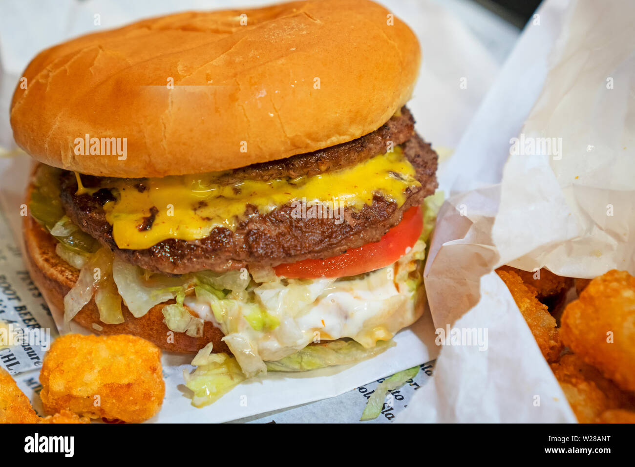 Cheesburger und Tater Tots sitzen auf dem Zeitungspapier - Typ menu mit einem Diner. Fast food Konzept. Fokus auf der Vorderseite des Burger Add-ons. Stockfoto