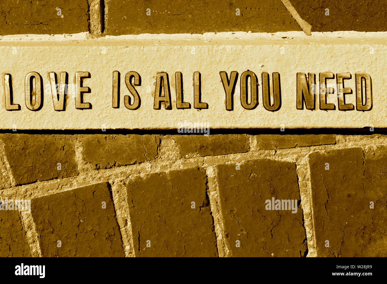 "Die Liebe ist alles, was Sie brauchen" Erklärung in Schrift erhaben auf einem Stein Hintergrund in Sepia close-up Stockfoto