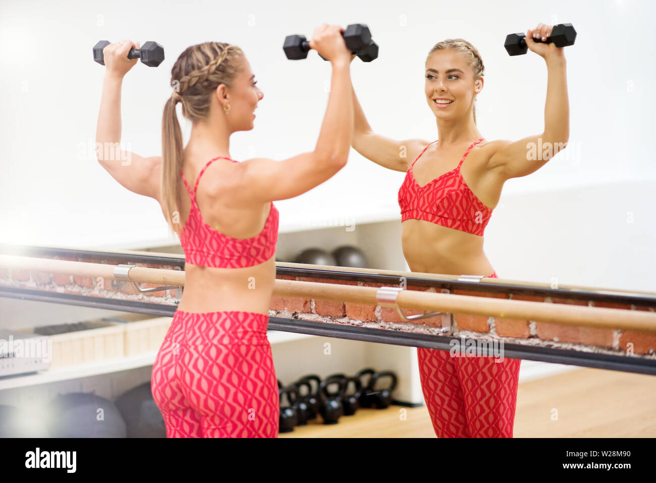 Junge passende Frau Ausübung Arme mit Hanteln vor Spiegel im Fitnessstudio Stockfoto
