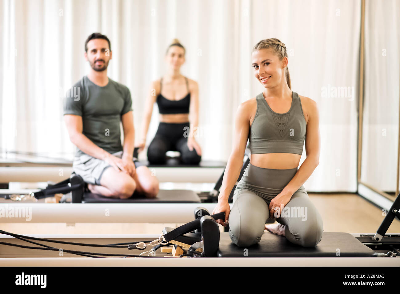 Drei junge Athleten auf Pilates Reformer Betten posiert im Fitnessstudio Stockfoto