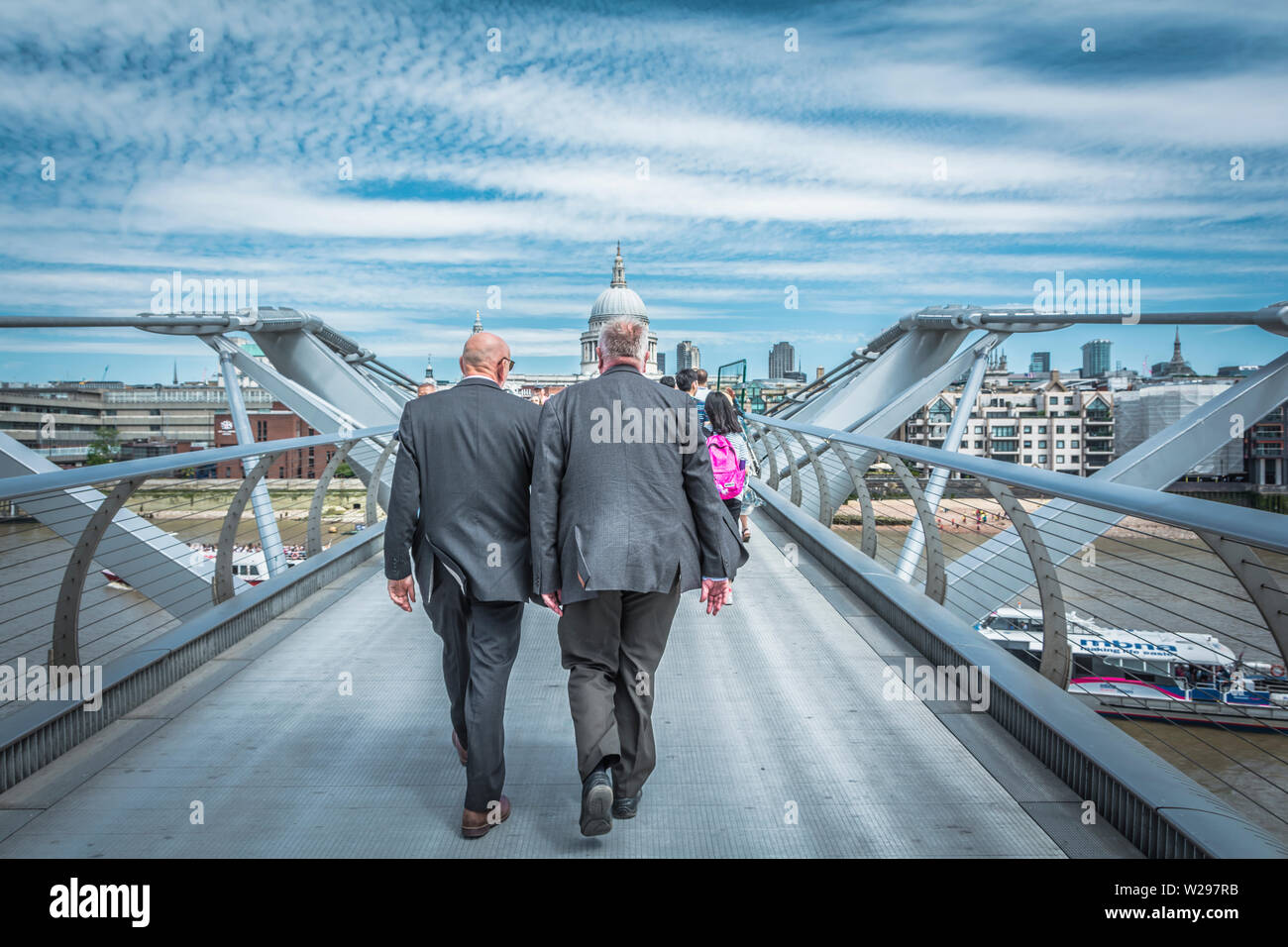 Zwei Männer mittleren Alters, in grauen Anzügen, gehen über die Millennium Bridge (Blade of Light), London, England, Großbritannien Stockfoto