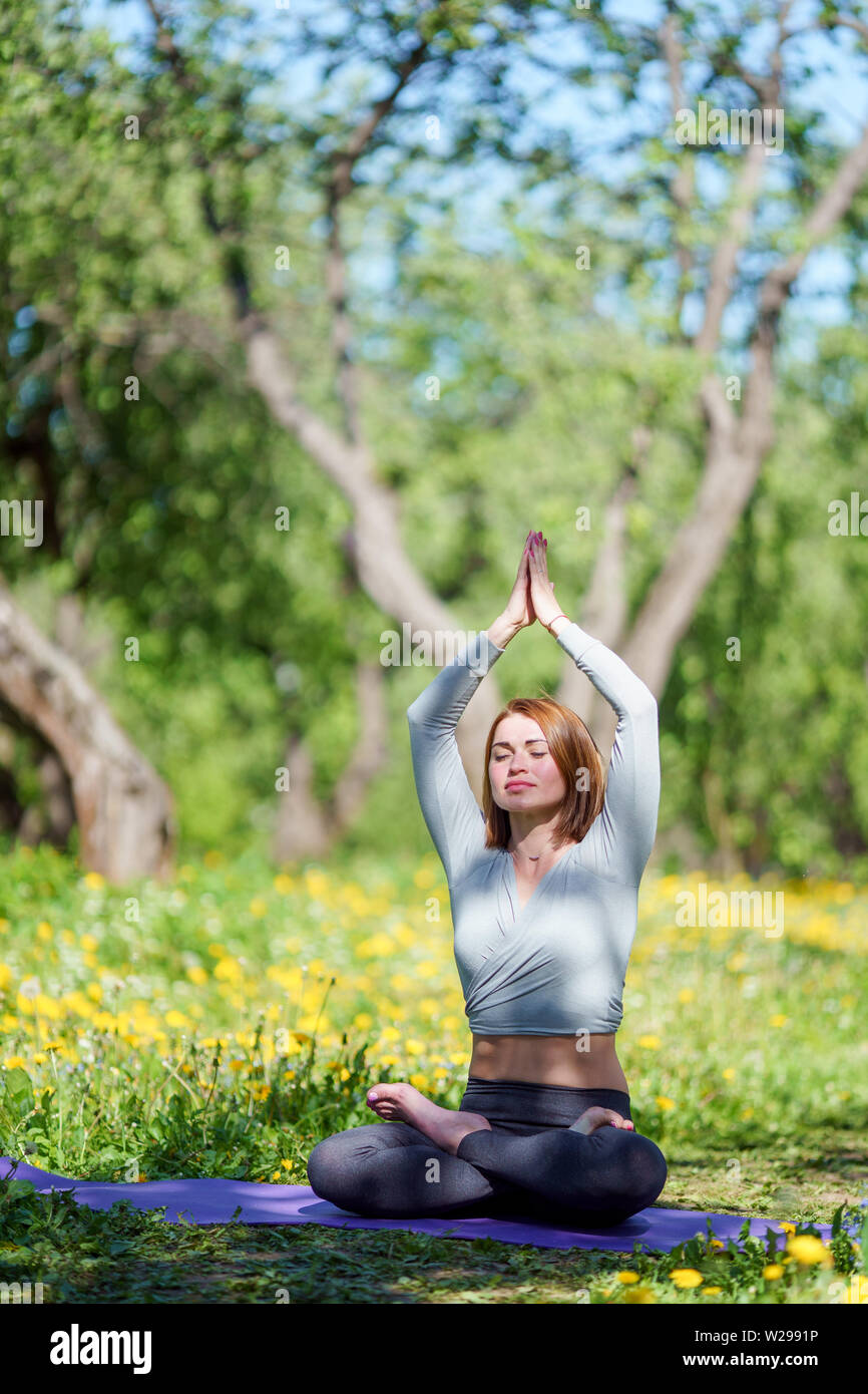 Das Bild der jungen Frau Yoga mit erhobenen Armen sitzen in Lotus Position auf blauen Teppich in Wald Stockfoto