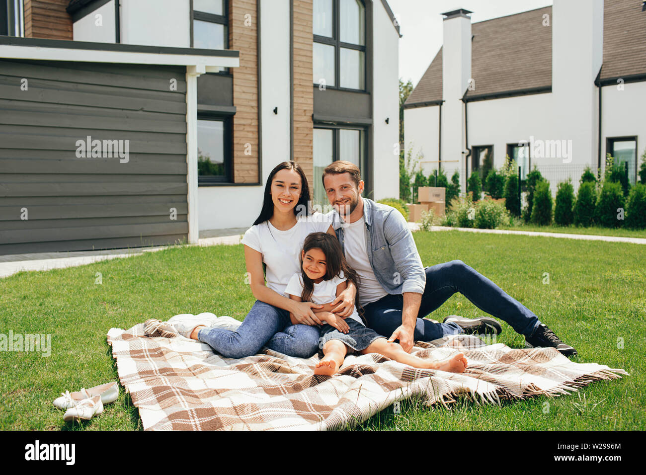Happy heteroseksual Familie sitzt auf Gras in der Nähe ihres neuen Hauses. Familie sitzt auf Rasen, Kauf neuer großes Haus. Stockfoto
