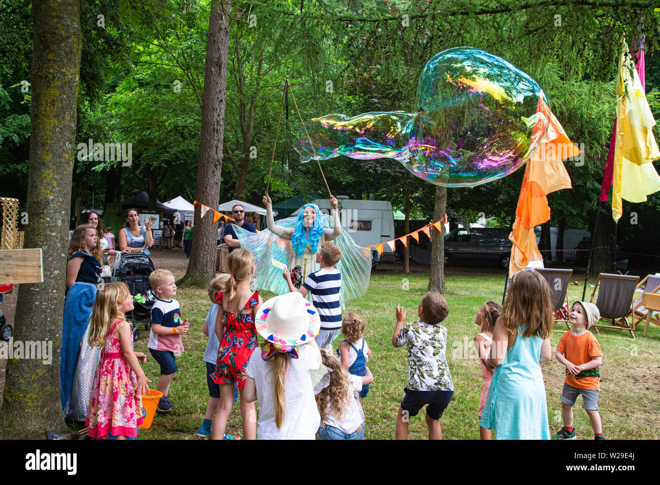90 Kent County zeigen, Detling, 6. Juli 2019. Einen blauen Haaren Märchen im Wald unterhält Kinder durch Blasen große Blasen.. Stockfoto