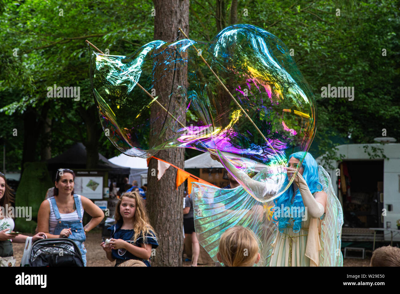 90 Kent County zeigen, Detling, 6. Juli 2019. Einen blauen Haaren Märchen im Wald unterhält Kinder durch Blasen große Blasen.. Stockfoto