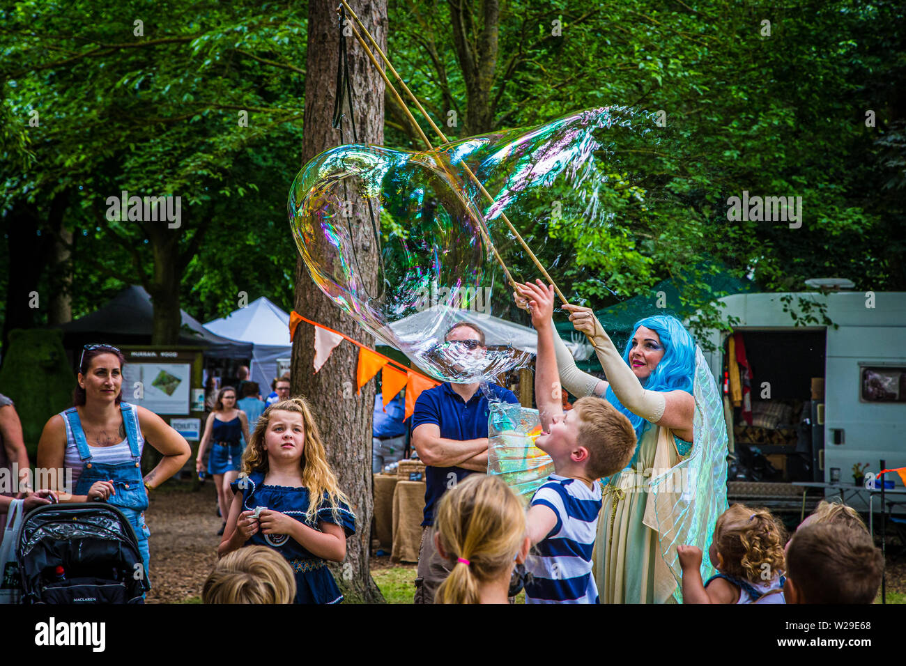 90 Kent County zeigen, Detling, 6. Juli 2019. Einen blauen Haaren Märchen im Wald unterhält Kinder durch Blasen große Blasen.. Stockfoto