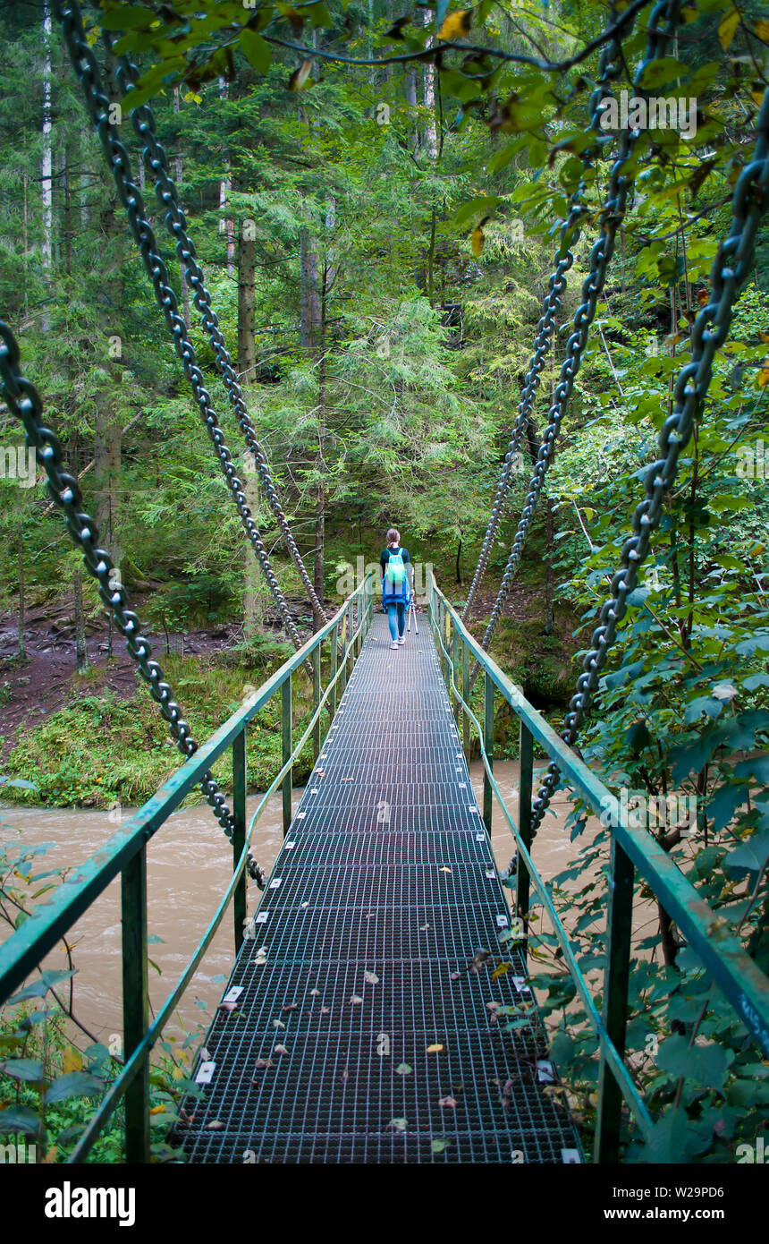 Zurück von einer jungen Frau auf einer metallenen Brücke über Fluss Hornad, Slovensky Raj. Hohe dunkelgrünen Kiefern, warmen Tag im September. Konzept der Abenteuer, activ Stockfoto