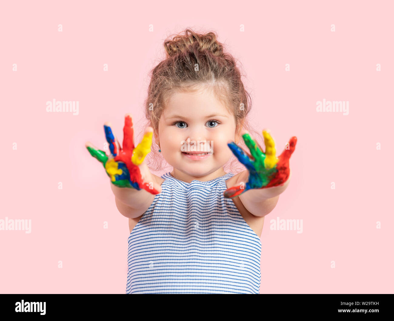 Lächelnde Mädchen mit Händen in der Farbe auf rosa Hintergrund. Stockfoto