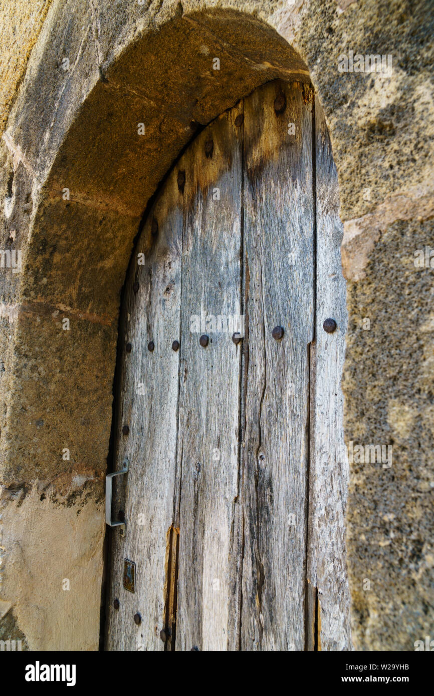 Verwitterte Holztür mit rustikalem Holz Korn, Nieten und ein Metall in einem Steinbogen Frame - Schrägansicht Griff, vertikale Ausrichtung im Hochformat Stockfoto