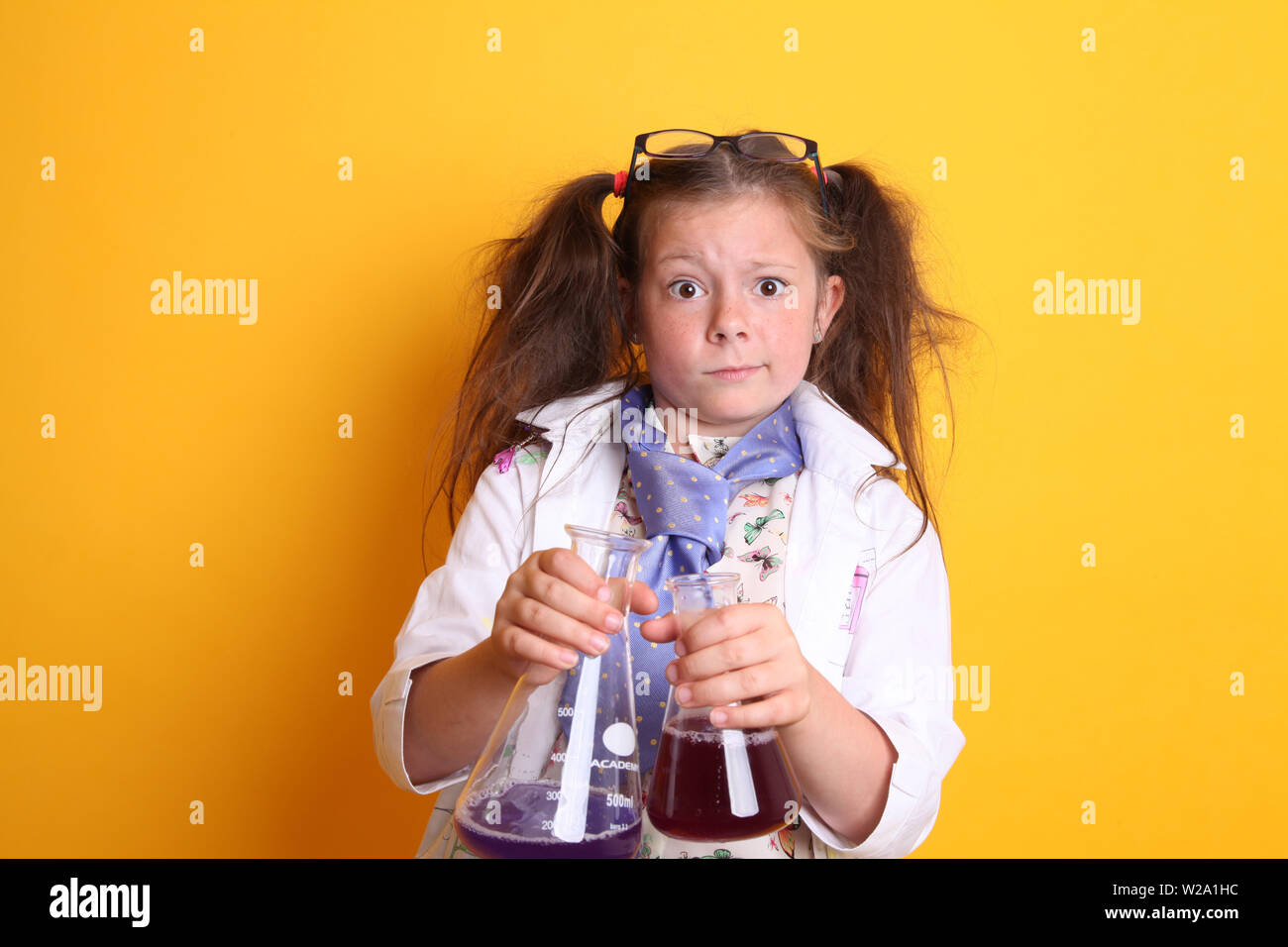MR - Science Experiment at Home Geek Young Girl Alter 7 - verrückt in der Kamera mit Borosilikatglas Wissenschaft Becher voller Chemikalien auf gelb Stockfoto