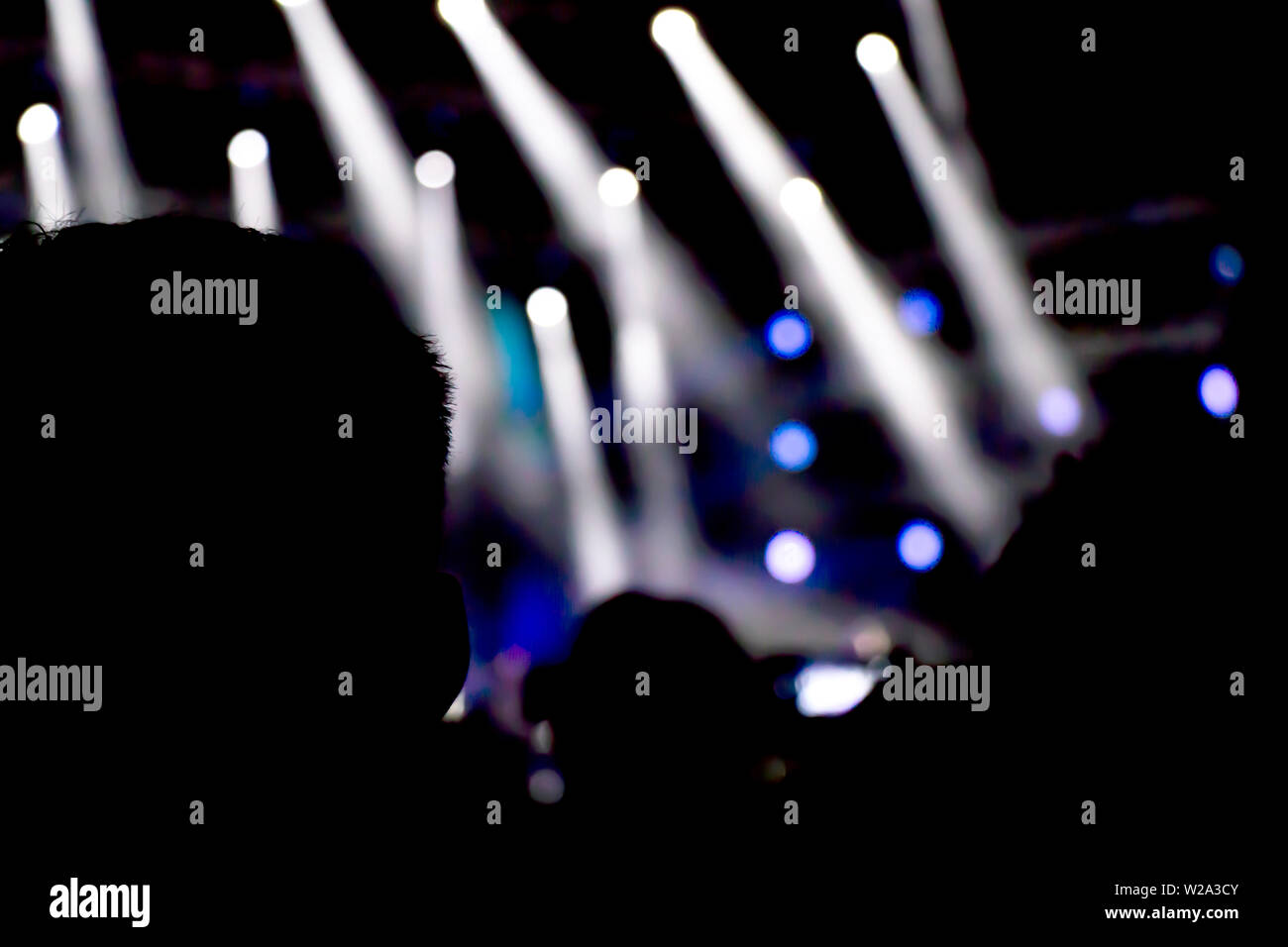 Silhouetten von Menschen beobachten das Konzert von hinten, mit Bühne Licht in der Ferne Stockfoto